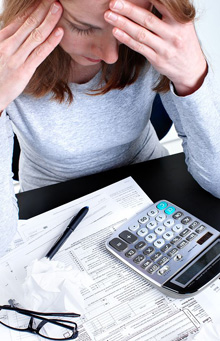 Woman with her head in her hands, tax forms and and a calculator trying to determine the best way to structure an offer in compromise. 