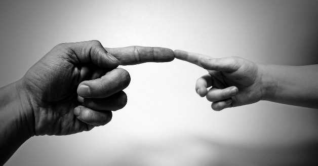 black and white photo of an adult man and child, hands only, index fingers touching 