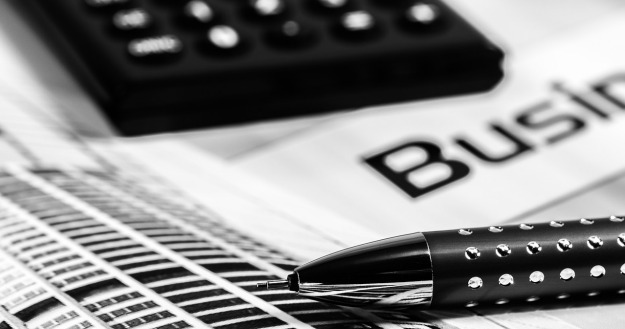 black and white photo of a calculator and fancy pen sitting on top of some business papers on the financial tools page 