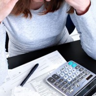 Woman trying to figure out an offer in compromise. Her head is in her hands, tax forms and and a calculator on the desk in front of her.